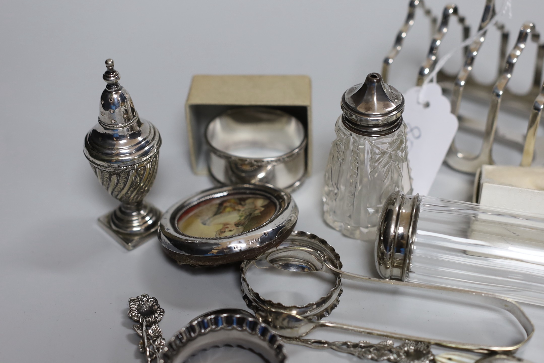 Assorted minor silver ware including a George V toast rack by James Dixon & Sons, 86mm, two napkin rings, a mounted glass toilet jar and condiment, pair of sugar tongs, a fruit knife, a commemorative spoon, a mounted sma